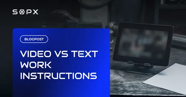 A tablet showing a work-instruction video beside a printed paper SOP on a dark workbench.